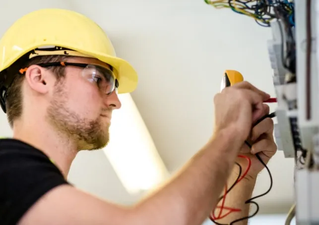 Electricista con casco y gafas midiendo con pinza amperimétrica en Málaga